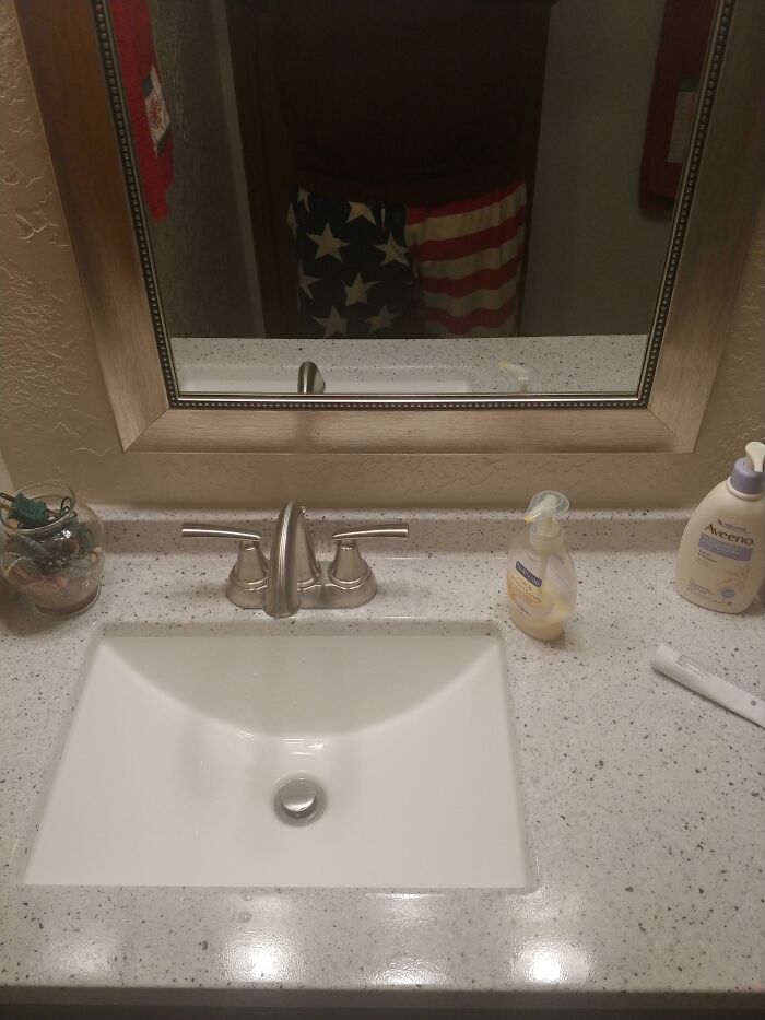 A bathroom vanity with a white sink and faucet. A reflection of American flag shorts in the mirror hints at potential home improvement fails.