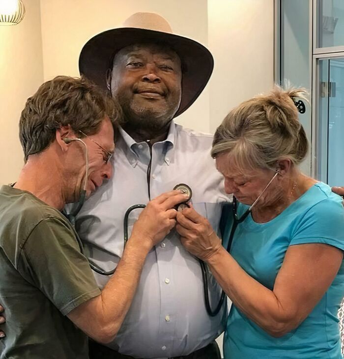Two people using stethoscopes on a man wearing a hat, symbolizing care and listening at Devil Sunrise event.