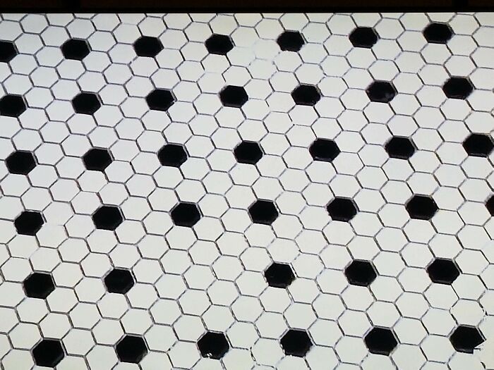 A bathroom floor with small hexagonal tiles, mostly white with a scattered pattern of black tiles, a potential home improvement fail.