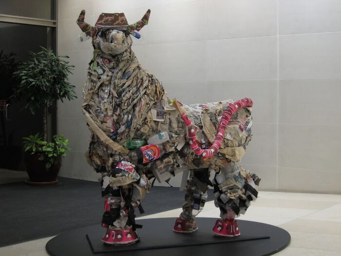 A large bull sculpture, creatively assembled from trash and recycled materials, showcasing useful artistic expression.