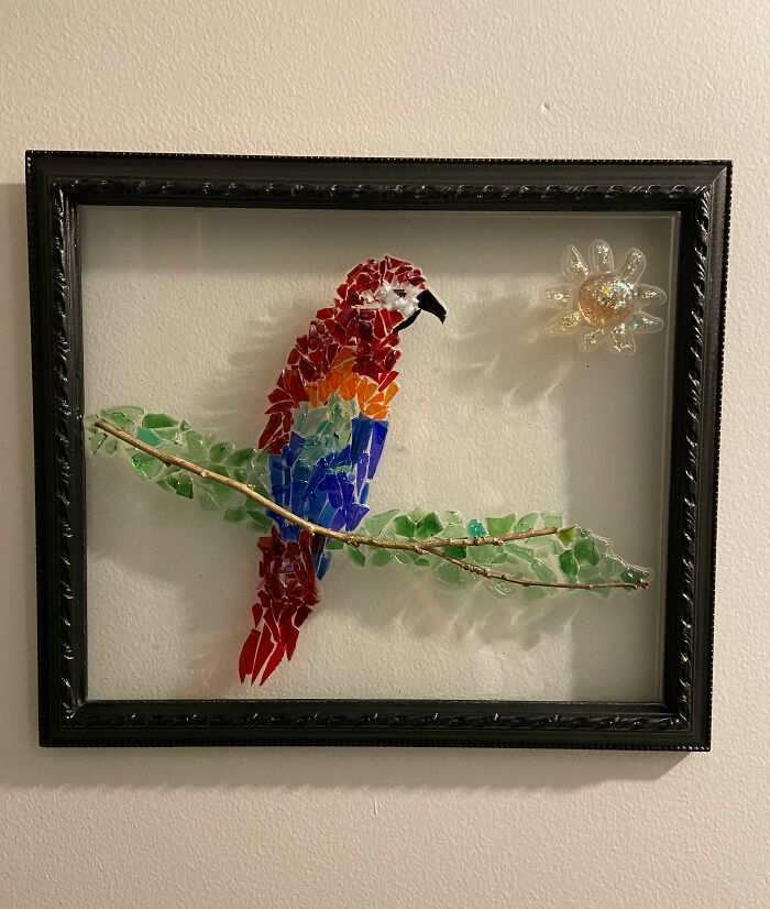 Artistic trash parrot mosaic framed with a branch and sun, showcasing how creative people use trash.