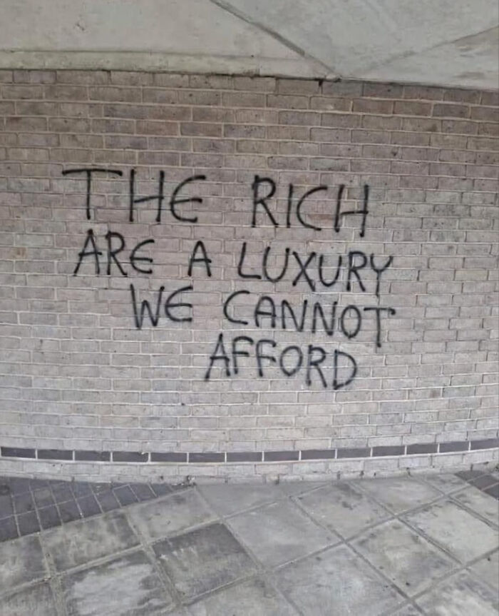 Graffiti on a brick wall reads: The rich are a luxury we cannot afford. Highlights that people can't afford billionaires.