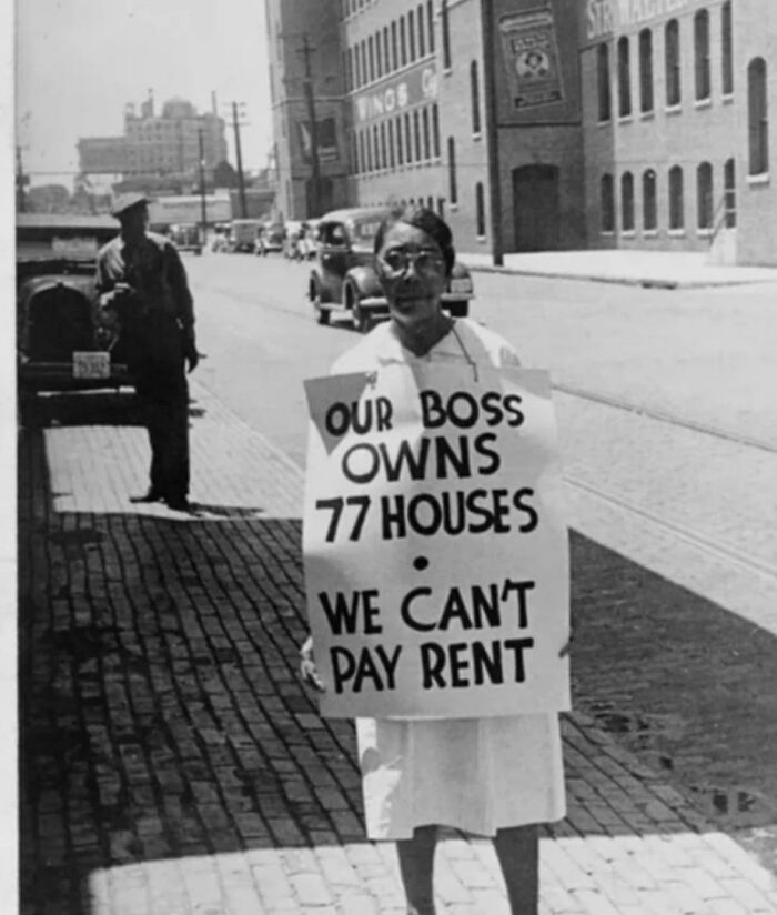 A person holds a sign stating, Our boss owns 77 houses, we cant pay rent, reflecting the struggle against billionaires.