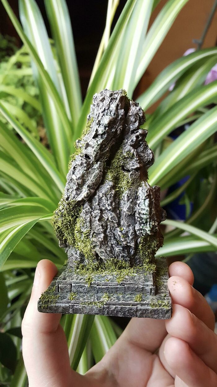 Hand holding a small, moss-covered trash rock sculpture, embodying creative people transforming trash into something artistic.