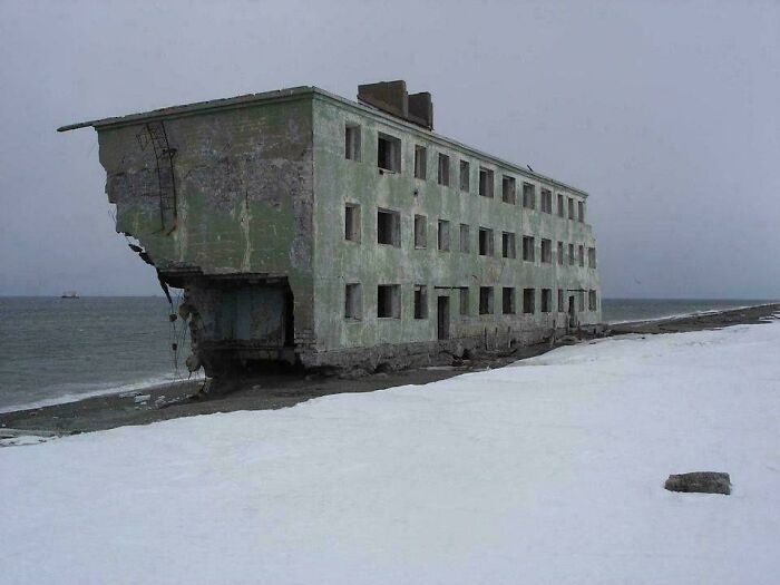Crumbling abandoned building on snowy shore in urban hell area