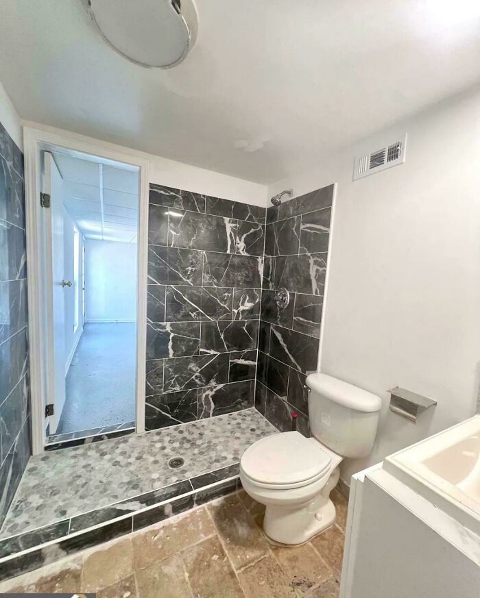 A messy bathroom with a new shower and toilet, but stained floor, resembling a home improvement fail. Concrete overflowed.