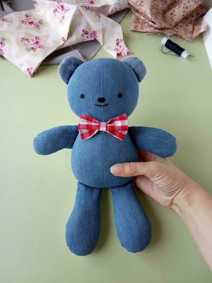 A hand holds a denim teddy bear with a red and white checkered bow tie. Creative people make something useful from trash.