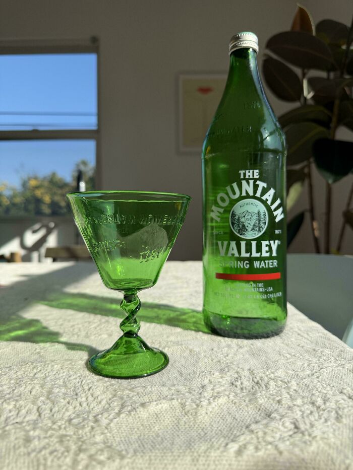 A green stemmed glass with a twist design sits next to a green Mountain Valley Spring Water bottle. Creative people turned trash into art.