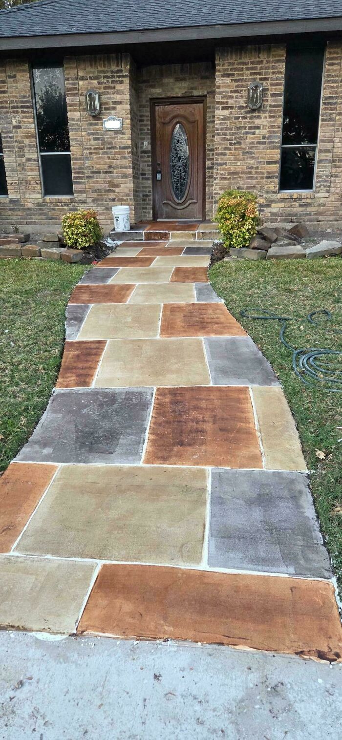 A house with a newly laid concrete walkway of colorful square and rectangular slabs. This home improvement project adds curb appeal.