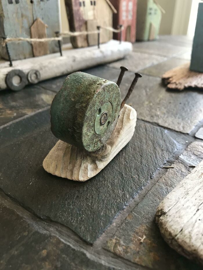 A snail figurine made from a creative trash upcycle: a green weathered metal cap for the shell and nails for antennae.