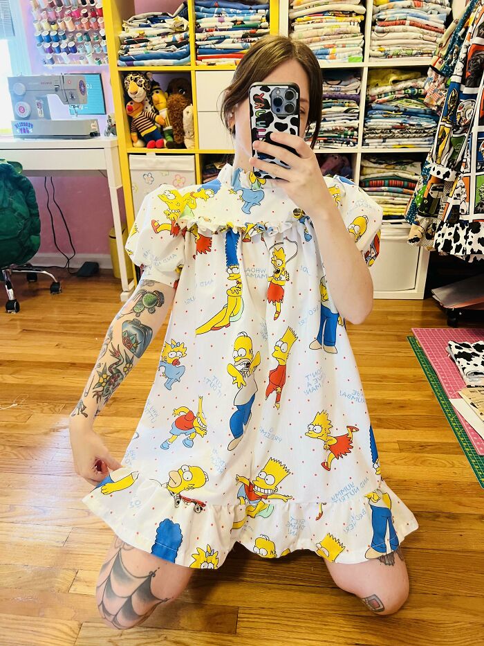 A person in a Simpsons print dress, with tattoos and a phone, showing creative clothing made from trash.