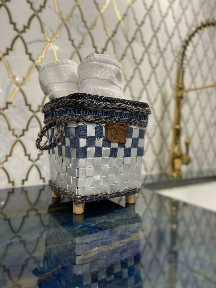 A creative person's woven trash basket made from denim and silver material, holding white towels, on a blue countertop.