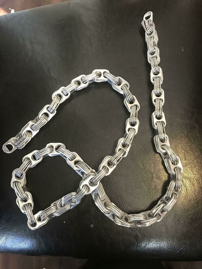 A chain-like creation made from recycled pull tabs on a dark surface, showcasing creative people turning trash into useful art.