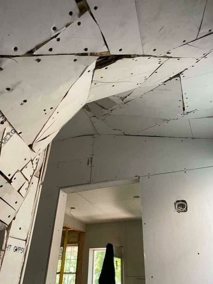 An extreme home improvement fail with a broken ceiling, featuring scattered drywall pieces and exposed studs in a room.