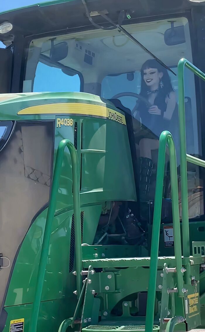 A person with dark makeup and clothing sits in a John Deere farm tractor, a sight that won't make sense to city kids.