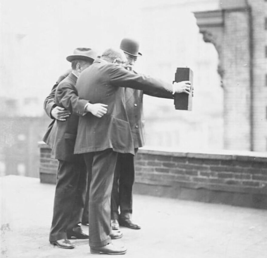 Three men in hats and suits taking a historic group photo, with one man holding the camera. Fascinating photos about history.