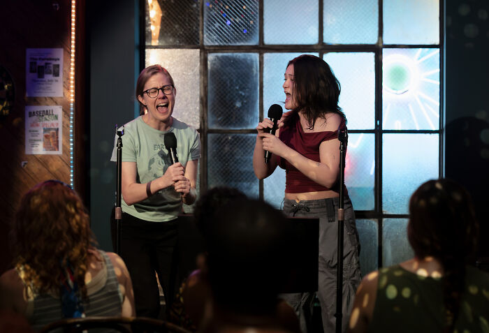 Two women performing on stage with microphones in front of an audience, related to The Pitt Season 3 updates.
