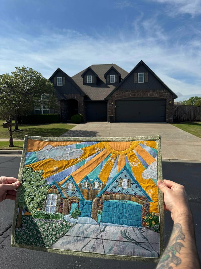 A person holding a handmade tapestry art of a house in front of the actual house, showcasing handmade projects.