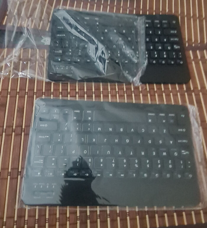 Two new black wireless keyboards in plastic wrap on a mat, highlighting orders from Temu or AliExpress.