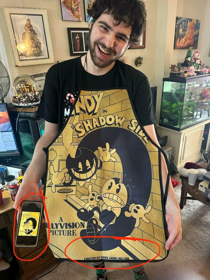 Smiling man holds a large Bendy cartoon apron, comparing it to the image on his phone. Likely a Temu or AliExpress order.