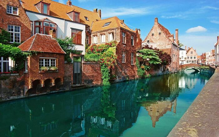 Breathtaking travel photos of historic brick buildings with red roofs lining a turquoise canal, reflecting on the water.