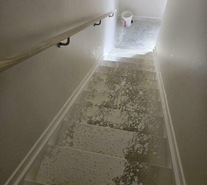 Concrete splashed across a white basement staircase, a home improvement fail. White bucket visible at bottom of stairs.