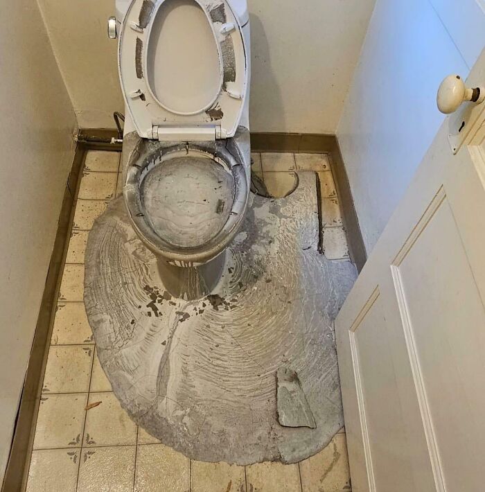A disastrous home improvement fail: concrete overflowed out of a toilet, covering the tiled bathroom floor.