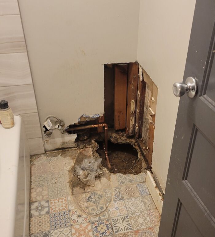 Home improvement fail: a bathroom wall damaged with exposed piping and dirt, floor tiles dirty.