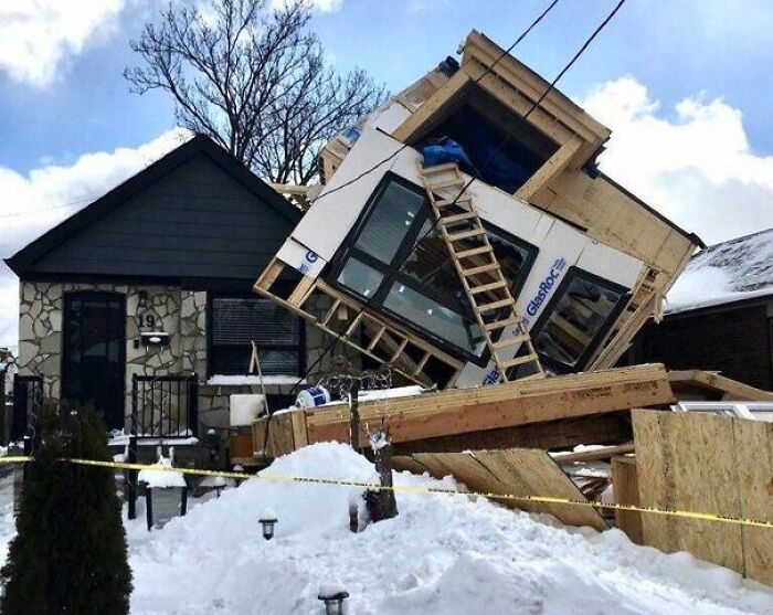 A home addition collapsing onto a house, surrounded by snow and yellow caution tape. A concrete home improvement fail.