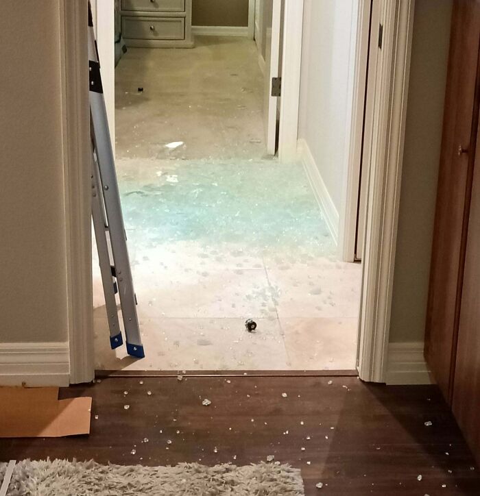 A hallway with a tile floor covered in shattered glass, leading to a room with a concrete overflow. Home improvement fails.