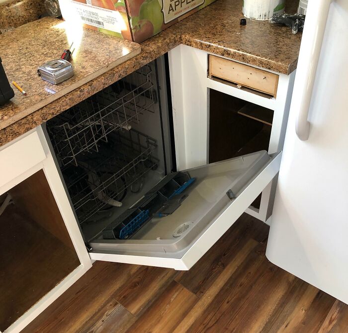 A kitchen in mid-renovation with an open dishwasher and unfinished cabinets, a definite home improvement fail.