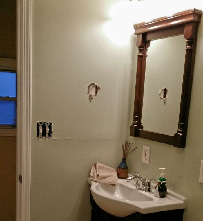 Bathroom wall damage from a disastrous home improvement fail, showing holes and exposed wiring next to a sink and mirror.