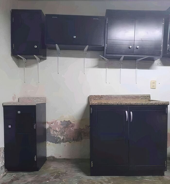 Home improvement fails: poorly installed dark kitchen cabinets with damaged walls, showing concrete overflow damage.