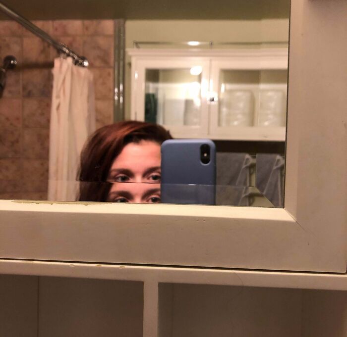 A person taking a selfie in a broken bathroom mirror, showing only their eyes. A home improvement fail.