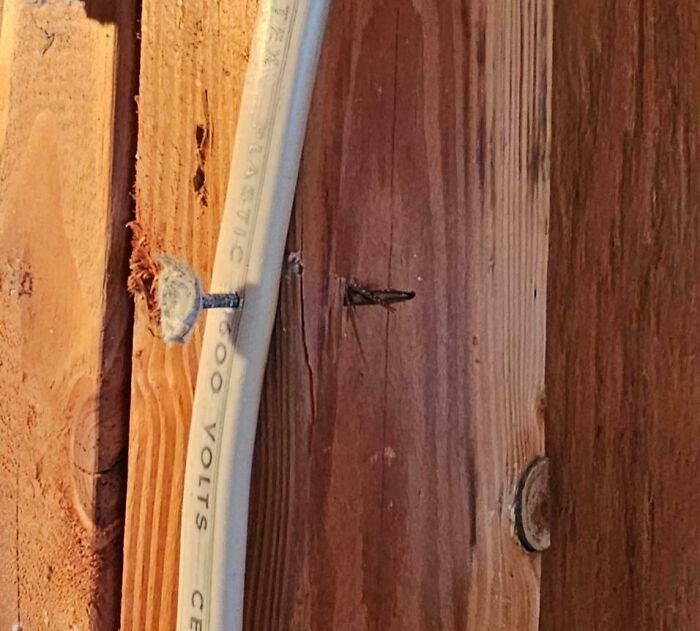 A nail dangerously piercing a white plastic electrical wire with "600 VOLTS" printed on it, a home improvement fail.