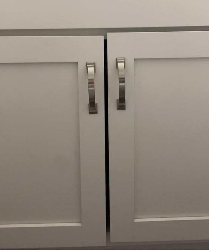 Misaligned gray cabinet doors with silver handles, highlighting a common home improvement fail in installations.