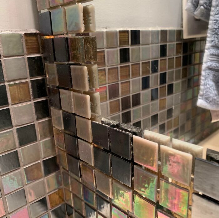 A corner of a mosaic tiled mirror, featuring unevenly placed, multi-colored tiles. A true home improvement fail.