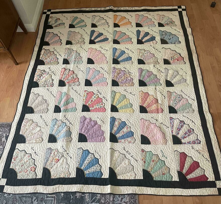 An antique quilt featuring colorful fan patterns and embroidered names, a suspicious good thing found in the Goodwill bins.