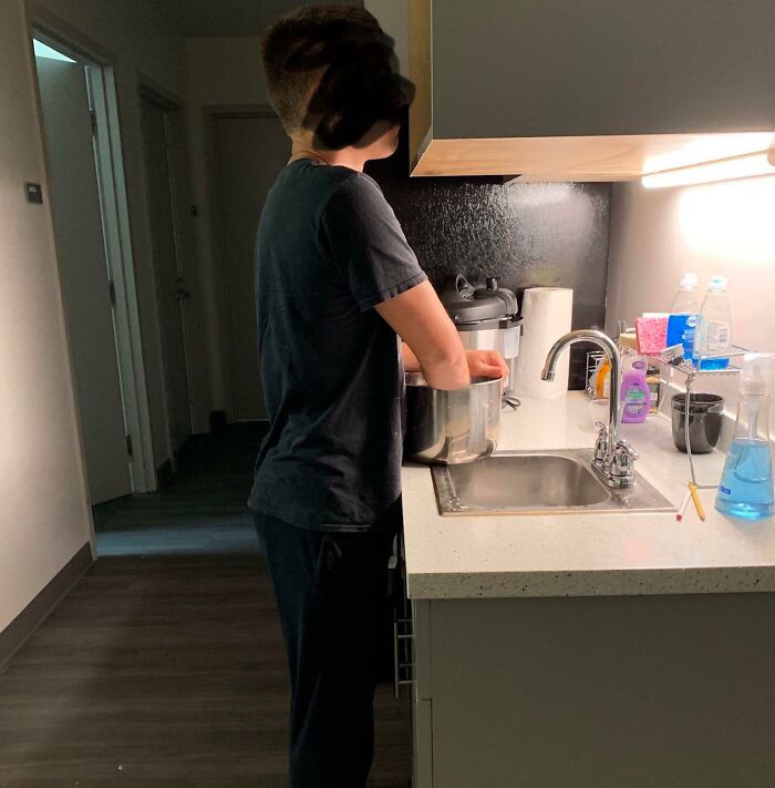 A person mixing something in a pot over a kitchen sink, a home improvement scene.