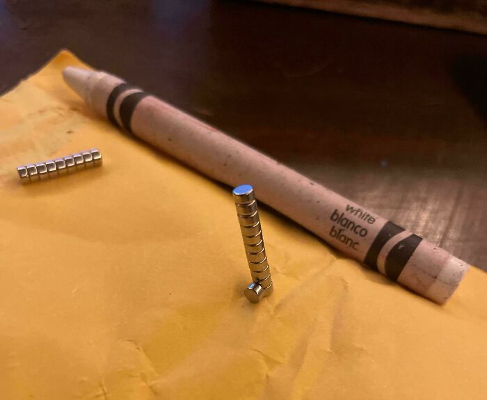 Two stacks of tiny cylindrical magnets next to a white crayon, depicting a surprising item ordered from Temu or AliExpress.