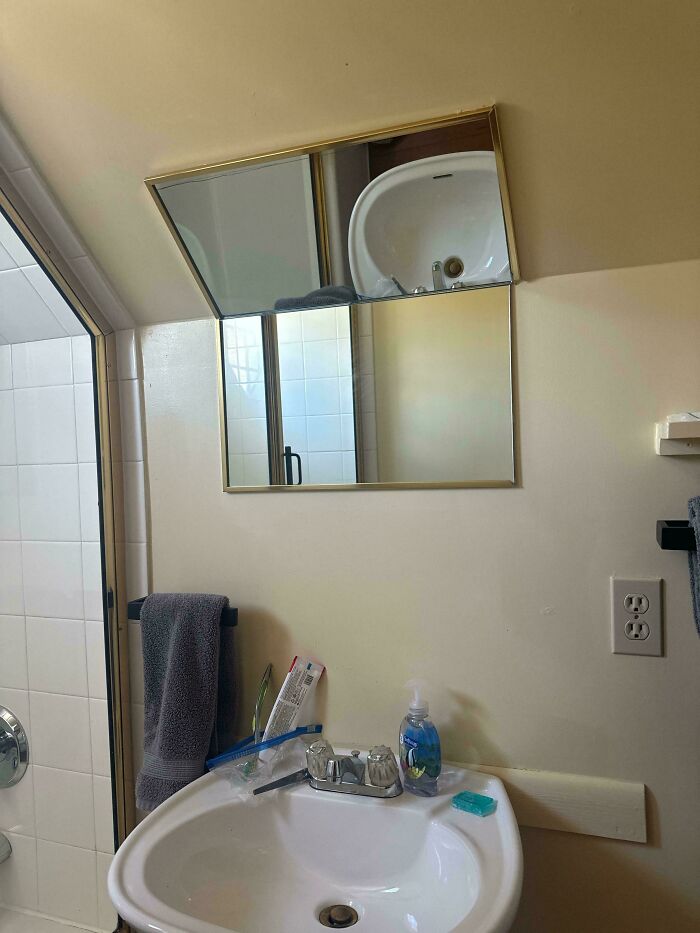 A slanted medicine cabinet mirror in a bathroom, reflecting an out-of-place sink. A home improvement fail.