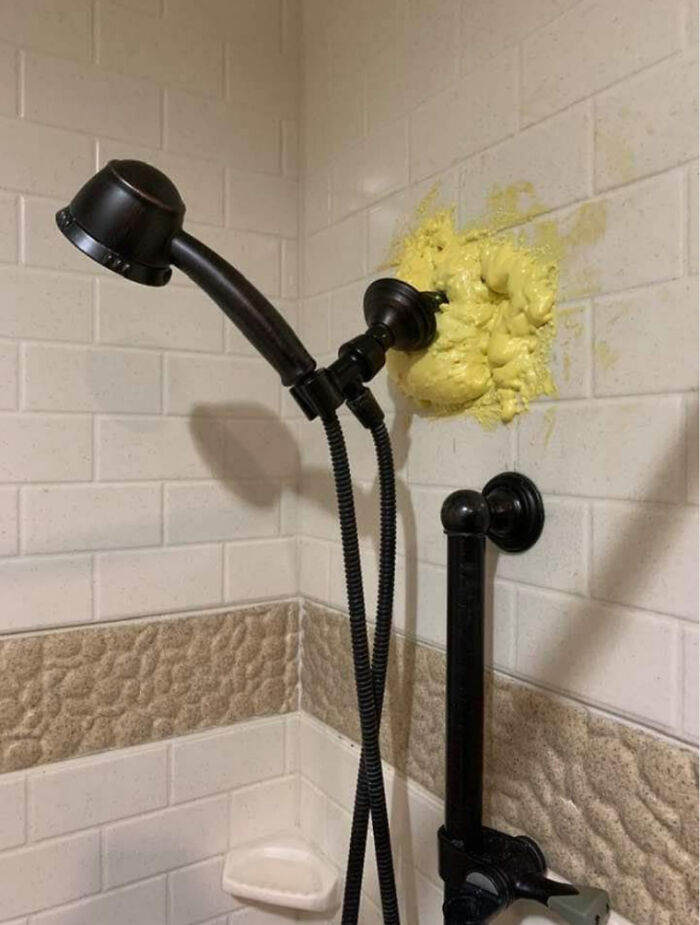 A showerhead mounted in a shower with white tiles, surrounded by bright yellow concrete overflowing from the wall.