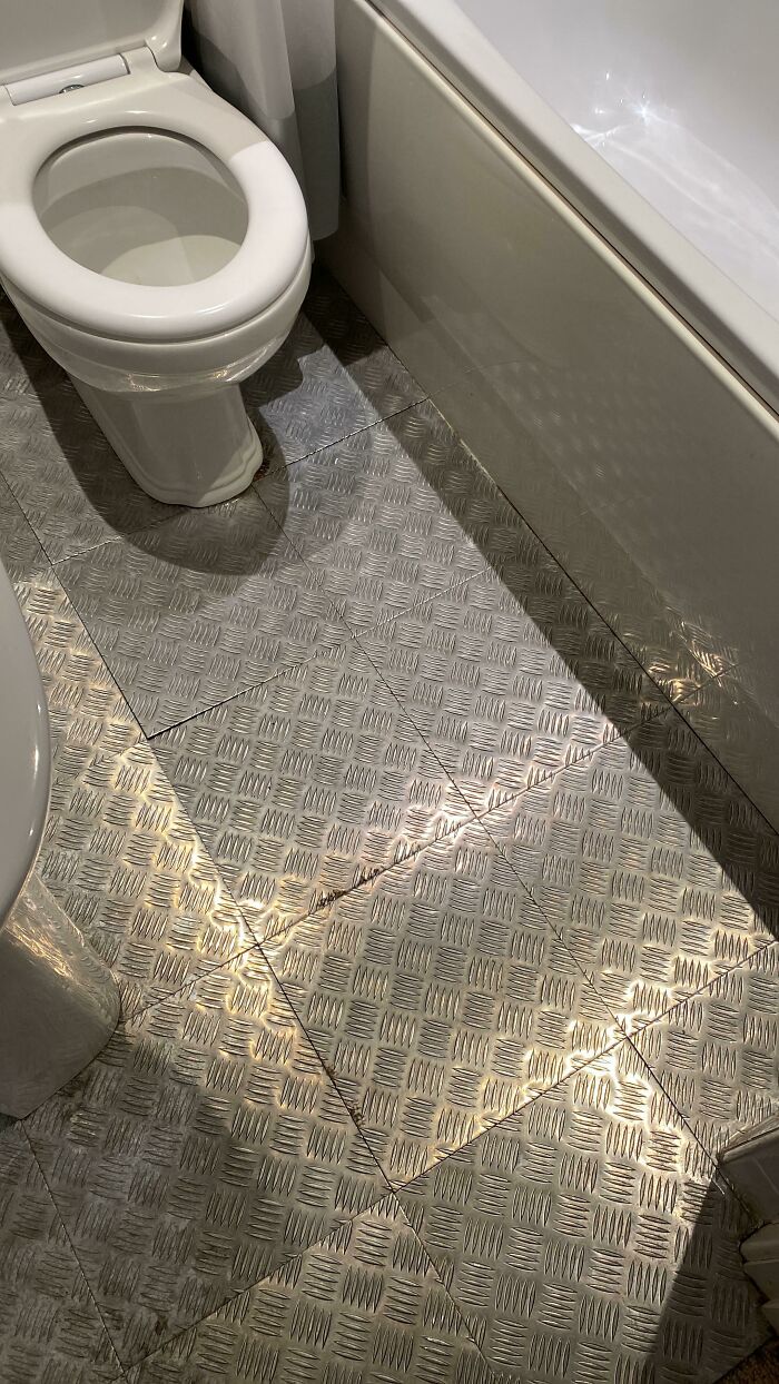 Close-up of diamond plate flooring in a bathroom with a toilet and bathtub. Home improvement fail.