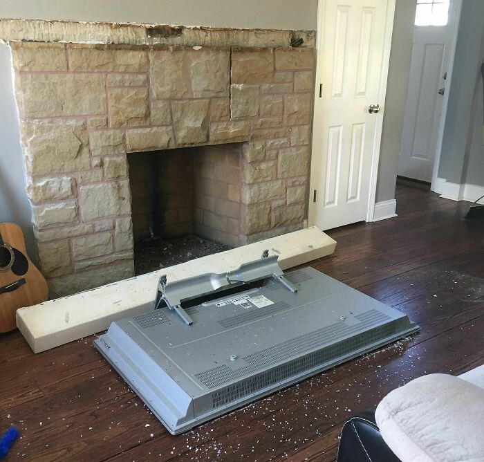 A fireplace with a TV face down on the wooden floor in a living room, a disastrous home improvement fail.