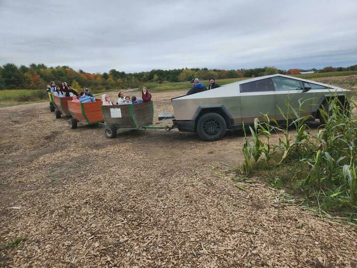 A futuristic Cybertruck tows two hayride wagons full of people on a farm, a sight that won't make sense to city kids.