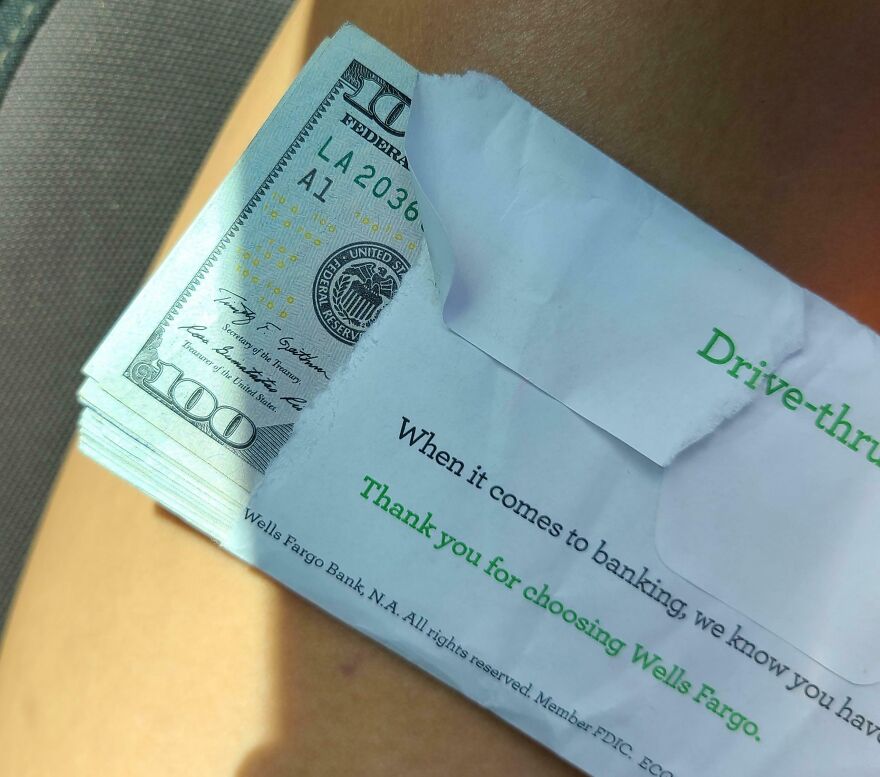 A stack of hundred-dollar bills peeks from a Wells Fargo envelope, hinting at something found in Goodwill bins.