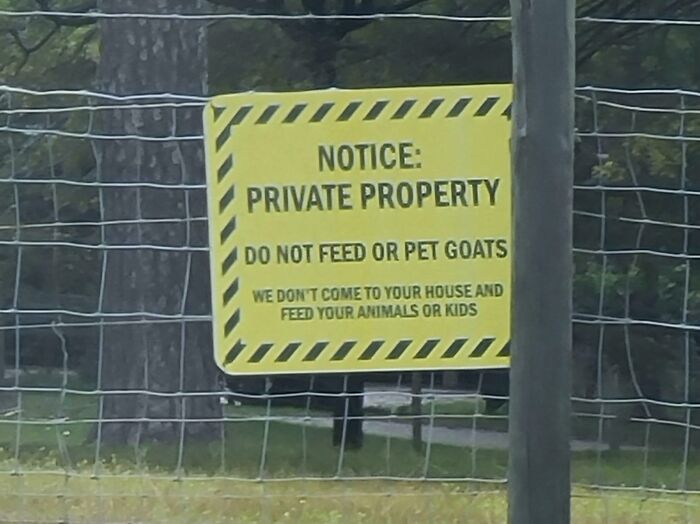A yellow sign on a fence, reading "NOTICE: PRIVATE PROPERTY DO NOT FEED OR PET GOATS." An example of oddly specific rules.