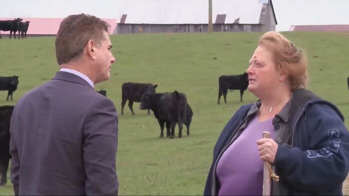 A man in a suit interviews a woman on a farm with cows grazing in a field, showing how life on a farm can be surprising.