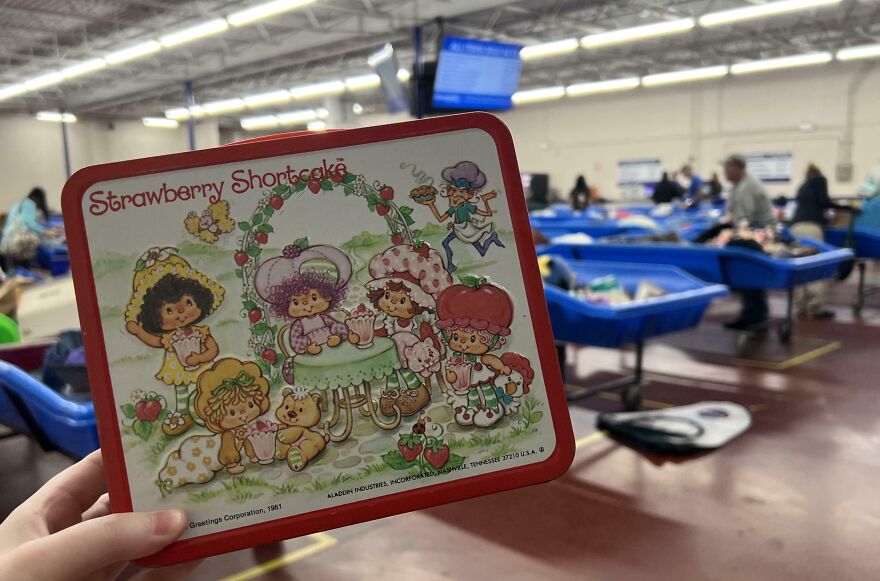 A person holding a vintage Strawberry Shortcake lunchbox found in the Goodwill Bins, a surprisingly good find.