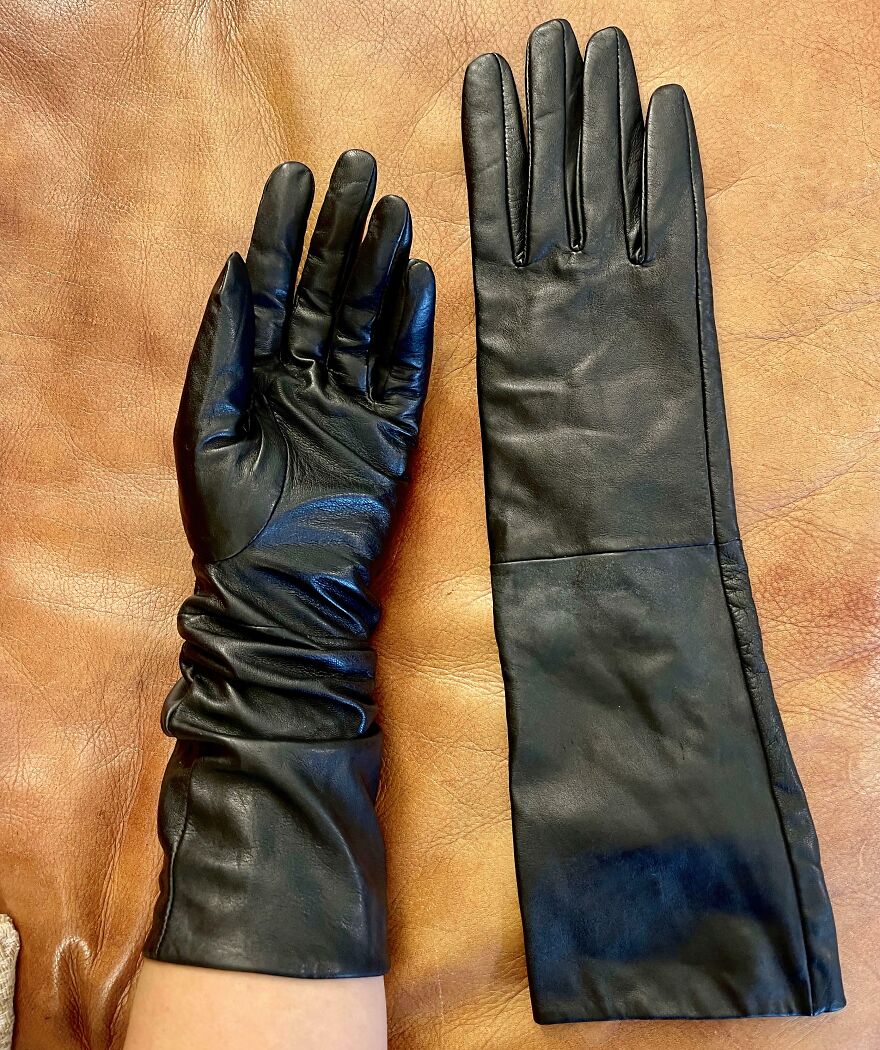 A pair of black leather gloves on a brown leather surface. These were actually found in the Goodwill Bins.